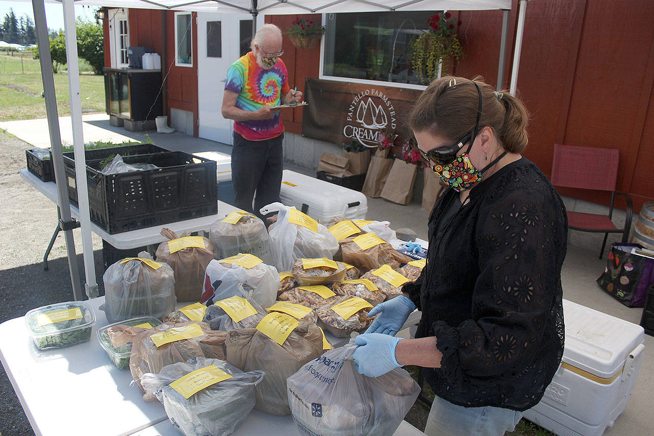 Everything you see on these tables have already been ordered, bought, and paid for by customers of the Enumclaw REKO Market, so all they have to do is drive up to the local Fantello Creamery to pick up their order. Pictured is REKO Market organizer Julie Kintzi in the flower mask and Steve Neason from Cedar Springs Farm, who was standing in for Cascadia Greens. Photo by Ray Miller-Still