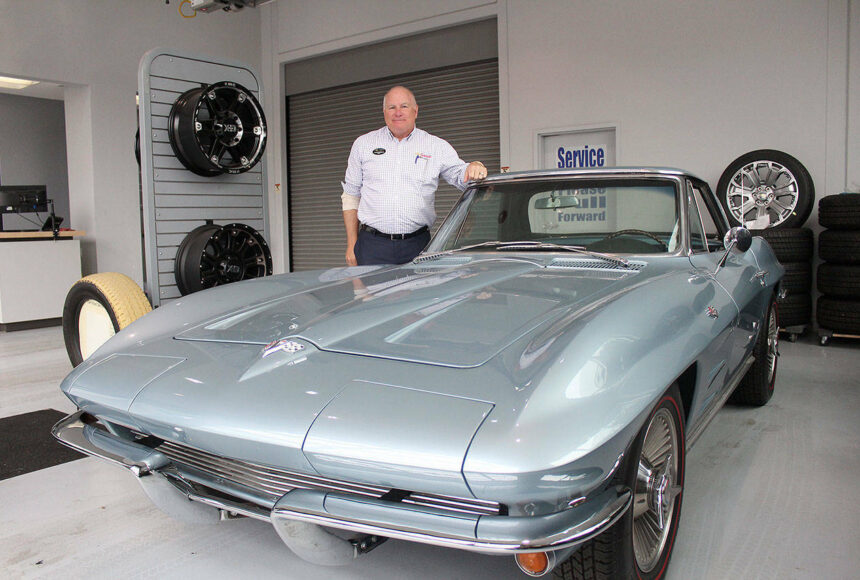 <p>Alan Gamblin, who took over his father’s dealership in 1985, stands in his car shop next to his personal 1964 Corvette in 2019 while celebrating being 50 years in business on the Plateau. Photo by Ray Miller-Still</p>